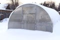 Winter greenhouse in the snow. The concept of care for plastic greenhouses in winter, snow removal