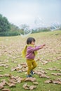 In winter, the ground is full of fallen leaves, and a child wearing a scarf plays on the green field Royalty Free Stock Photo