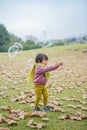 In winter, the ground is full of fallen leaves, and a child wearing a scarf plays on the green field Royalty Free Stock Photo