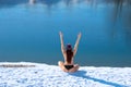 Winter hardy woman back view body with raised hands up on snow - white bank of the blue lake background copy space