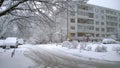 Winter is here. Snowfall in the city. White snow covered tree, cars and road near apartment residential building. Chilly. Cityscap