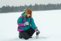 Winter hiker woman with metal drink flask taking break at snowy landscape background