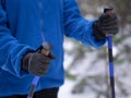 Winter hiking, details. Human hands with handles of nordic walking sticks. Person in blue sweatshirt make movement