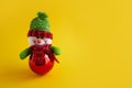 Winter holiday concept snowman in a christmas hat and scarf christmas toy on a yellow background place for text Royalty Free Stock Photo