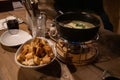 Rustic tablescape. Traditional French cheese fondue in hot pot and white bowl with bread crackers. Utensil atop wooden table. Royalty Free Stock Photo