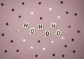 Winter Holiday Layout with Wooden Blocks with `Ho Ho Ho` and Glowing Confetti of Star Shape on a Light Pink Background. Royalty Free Stock Photo