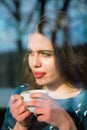 Winter holidays, christmas, hot drinks concept. Happy beautiful young woman drinking coffee behind a window. Vertical image Royalty Free Stock Photo