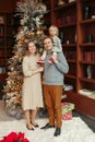 Winter holidays with family. Smiling Caucasian mother and father with baby girl daughter standing by decorated Christmas tree at Royalty Free Stock Photo