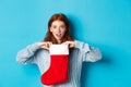 Winter holidays and gifts concept. Funny redhead girl looking surprised, open Christmas stocking and smiling, receiving Royalty Free Stock Photo
