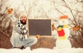 Winter holidays. Guy and snowman snowy nature background. Winter event. Upcoming event. Man with beard hold chalkboard