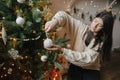 Winter holidays preparations. Happy woman in cozy sweater decorating christmas tree with modern white bauble. Young female holding Royalty Free Stock Photo