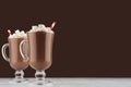 Winter hot drink cocoa with marshmallows and red striped straw on dark brown wall, white wood table, copy space.