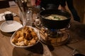 Rustic tablescape. Traditional French cheese fondue in hot pot and white bowl with bread crackers. Utensil atop wooden table. Royalty Free Stock Photo