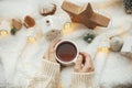 Winter hygge flat lay. Hands holding stylish cup of tea with modern cute christmas houses, pine cone, wooden star and tree, golden Royalty Free Stock Photo