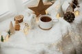 Winter hygge. Stylish cup of tea with modern cute christmas houses, pine cone, wooden star and tree, golden lights on soft warm Royalty Free Stock Photo