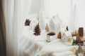 Winter hygge. Stylish cup of tea with modern cute christmas houses, pine cone, wooden star and tree, golden lights on soft warm Royalty Free Stock Photo