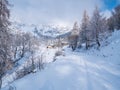 Winter in the italian Alps. Beautiful view of idyllic village in snowy forest and snowcapped mountain peaks. Piedmont, Italy Royalty Free Stock Photo