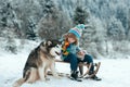 Winter knitted kids clothes. Boy sledding in a snowy forest with dog husky. Outdoor winter fun for Christmas vacation. Royalty Free Stock Photo