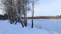 In winter, the lake is covered with ice. Along the shore there are birch trees and a path with footprints in the snow. On the oppo