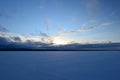 Winter lake covered with ice in white snow under the twilight light from the clouds in the blue frosty sky Royalty Free Stock Photo