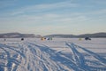 Trace from cars on a snowy big lake with fishermen in the background.