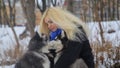 Winter landscape with blonde girl playing with siberian husky malamute dogs outside.