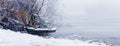 Winter landscape with a boat on the river bank, snowy trees in the fog Royalty Free Stock Photo