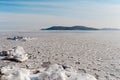 Winter landscape, cold frozen sea covered with small round icicles, blue clear sky against the backdrop of mountains and hills