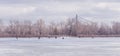 Winter landscape with a frozen river, ice fishing fishermen and a bridge behind the trees Royalty Free Stock Photo