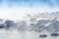 Winter landscape of lake with misty surface. Rocks on river bank are covered with snow