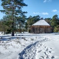 Winter landscape with a large historic sheep pen next to a pine tree behind a snowy footpath