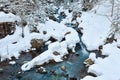 Winter landscape of a mountain river, the water slowly flows down the river bed between snow-covered stones Royalty Free Stock Photo