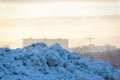 A mountain of snow against the backdrop of a sunset, cityscape and tower crane