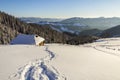 Winter landscape of mountain valley on frosty sunny day. Footprint path in white deep snow leading to small old wooden shepherd