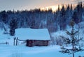 Winter landscape with an old abandoned house covered with snow on the backdrop of a winter snowy forest and sunset Royalty Free Stock Photo