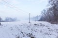 Winter landscape with power line, clearing in the forest covered with snow on a foggy day Royalty Free Stock Photo