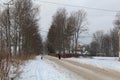 Elderly woman on the winter road. The dog accompanies the woman. Badly cleaned. Dirty road. It`s hard to go.