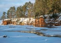 Winter landscape with red sandstone cliffs on the bank of the river Salaca, the sun shines on the trees and the river bank, the