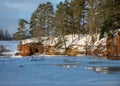 Winter landscape with red sandstone cliffs on the bank of the river Salaca, the sun shines on the trees and the river bank, the