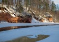 Winter landscape with red sandstone cliffs on the bank of the river Salaca, the sun shines on the trees and the river bank, the Royalty Free Stock Photo