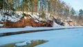 Winter landscape with red sandstone cliffs on the bank of the river Salaca, the sun shines on the trees and the river bank, the Royalty Free Stock Photo