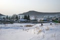 A rustic winter landscape with walking children and a frozen river in the foreground.