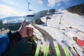 Hand with thumb-up gesture and skis on background of mountain ski-lift rope way on winter day. Royalty Free Stock Photo