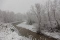 Winter landscape with snow coming down and a river in the middle of trees covered by snow Royalty Free Stock Photo