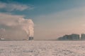 Winter landscape with snow covered frozen ice, city and pipes with thick steam