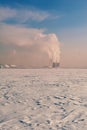 Winter landscape with snow covered frozen ice, city and pipes with thick steam