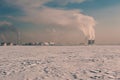 Winter landscape with snow covered frozen ice, city and pipes with thick steam