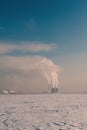 Winter landscape with snow covered frozen ice, city and pipes with thick steam