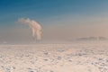 Winter landscape with snow covered ice, city and pipes with thick steam