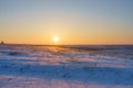 Winter landscape with snow covered plain, blue sky and orange sun at sunset. Beautiful natural scenic background Royalty Free Stock Photo